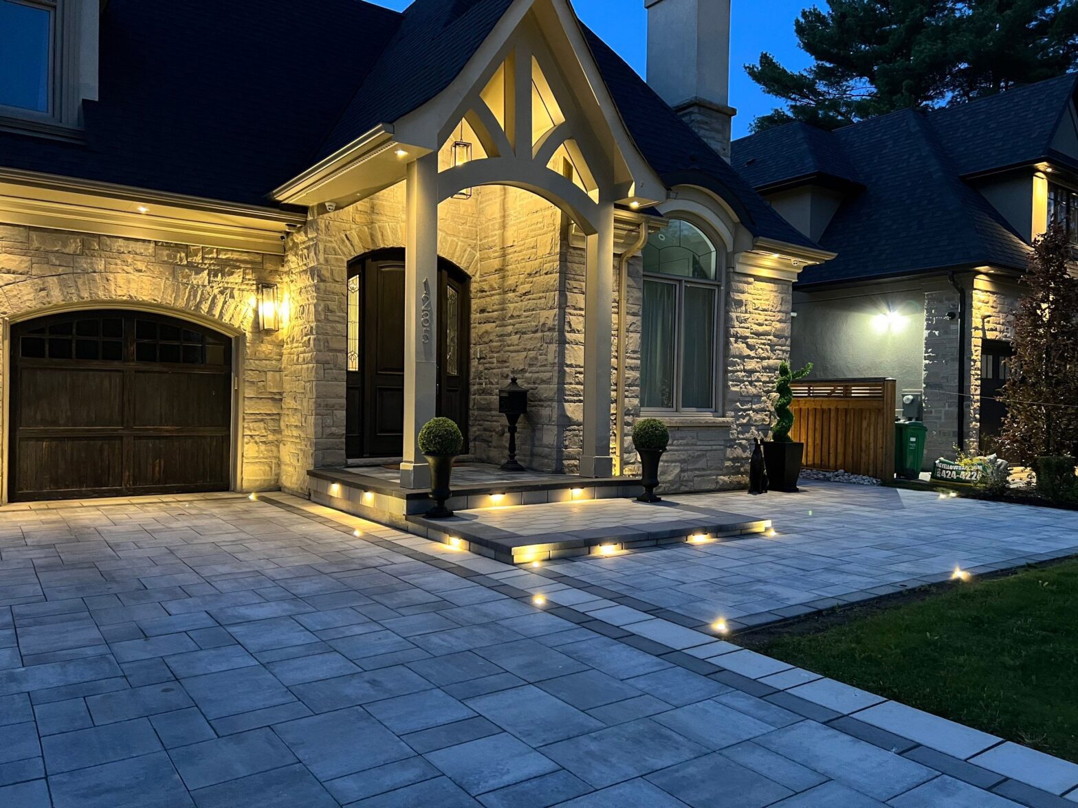 Elegant front entrance with grey interlocking stone, step lighting, and a stone façade.