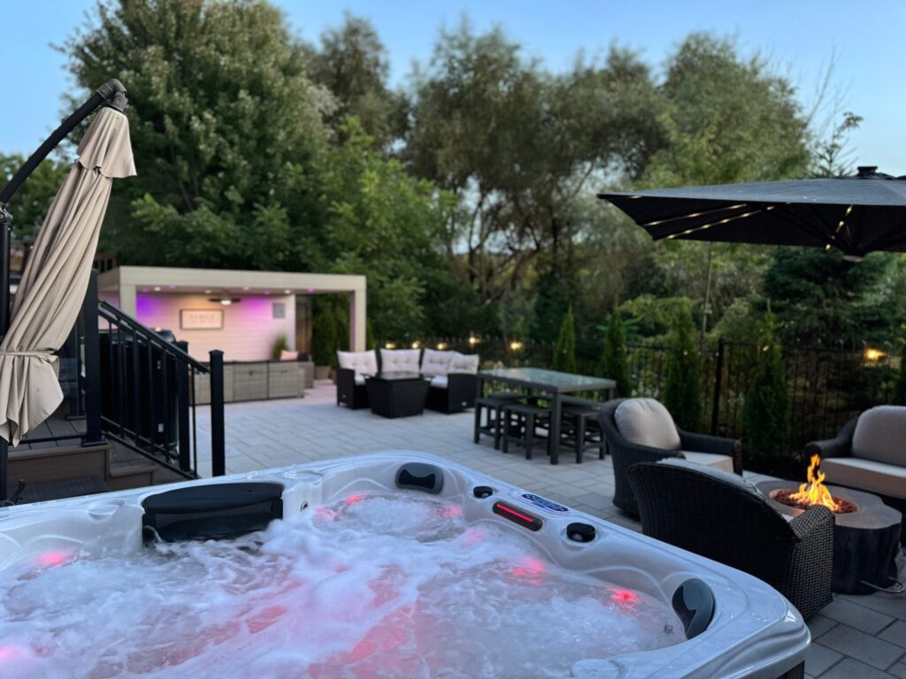 Cozy backyard with a hot tub, fire pit, modern lounge area, and grey interlocking stone patio.